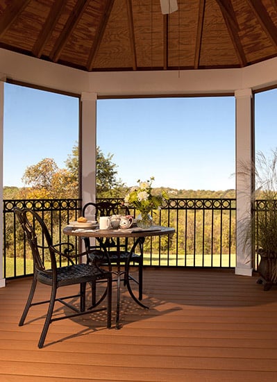 A covered deck with a bistro style table and chairs with a tea setting and vase of flowers.