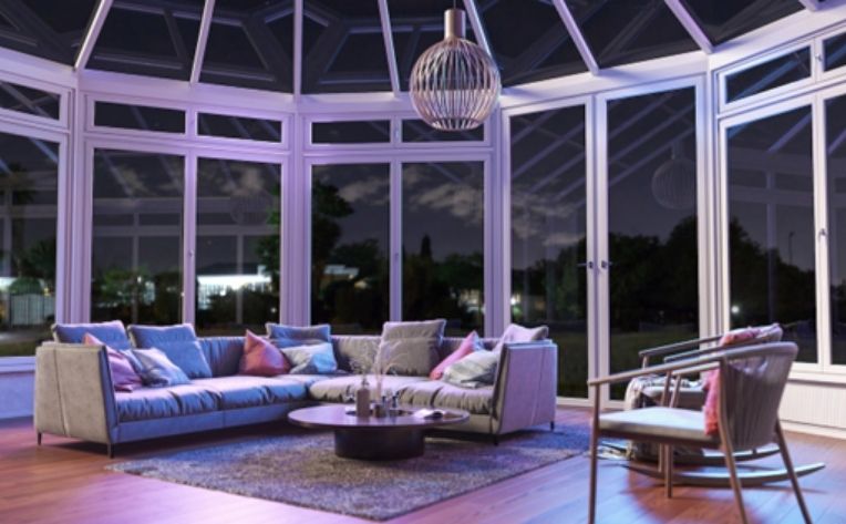 Elegant sunroom with floor-to-ceiling windows, vaulted glass ceiling, comfortable seating, and a modern chandelier.