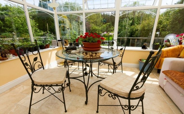 A solarium with metal black chairs and red flowers on the table