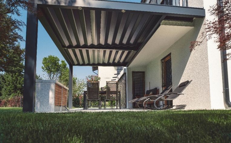 Modern backyard patio featuring a sleek black aluminum pergola with an integrated louvered roof system over a dining area and outdoor kitchen unit.