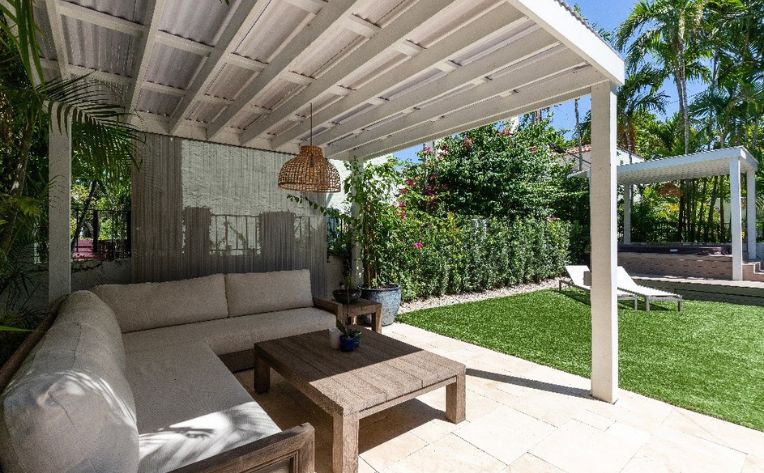 Backyard of a white house with a patio cover and a center table with plants all around