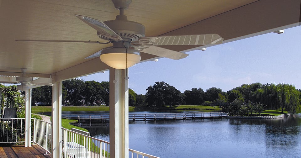 A covered patio with a fan overlooking a lake. 