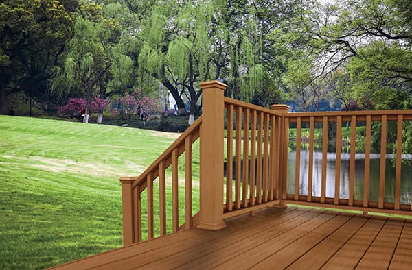 A wooden deck with railing overlooking a pond, green grass, and willow trees.